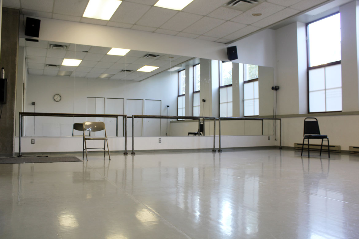 The dance studio at MAI. A room with a mirrored wall and warm-up bars, covered dance floor, large windows on on wall
